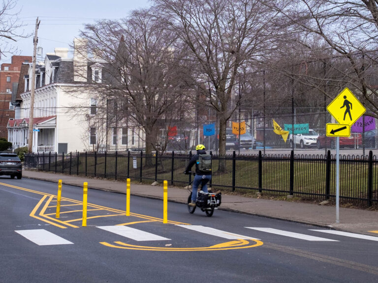 A person biking past a quick-build midblock crossing with flexposts and pavement markings.